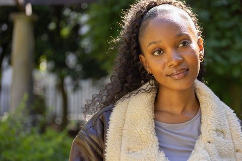 Sunlit african american woman in twenties in shearling jacket gazing thoughtfully in garden