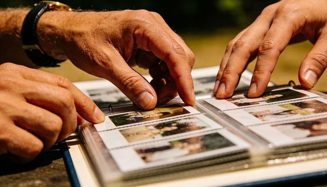 Senior hands pointing through vintage family album outdoors, sharing nostalgic memories