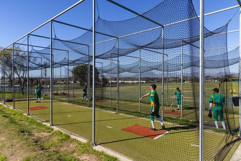 Cricket players training in net cages on suburban turf practicing batting and bowling