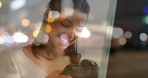 Smiling Woman Checking Camera Display with Night Bokeh Reflections