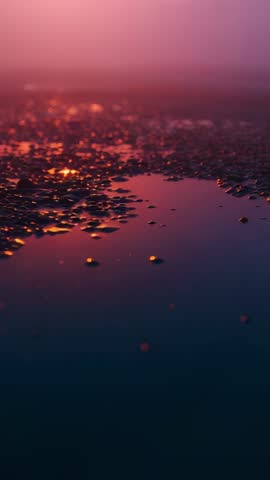 Vertical sunset shoreline reflecting puddle shimmering over pebbles with misty bokeh and ripples