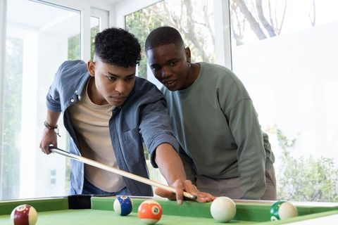 Hispanic and african american teenagers playing pool in sunlit home lounge