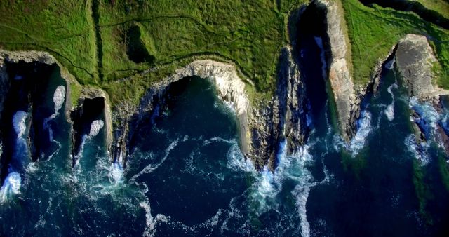 Aerial view of rugged coastal cliffs with natural arches carved by the ocean. The dynamic interaction between land and water creates a dramatic and scenic landscape.