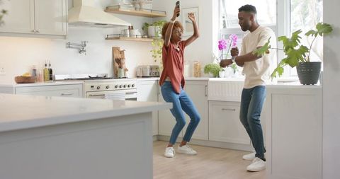 Joyful couple dancing in modern sunlit kitchen sharing music, coffee and morning energy