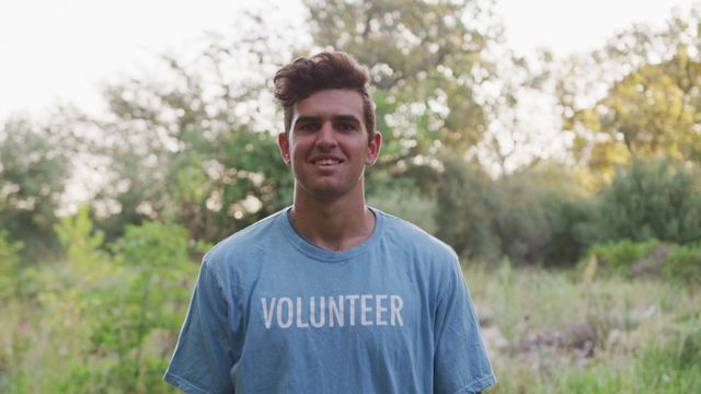 A male Caucasian volunteer is smiling while cleaning up a river in the countryside. Excellent for campaigns about community service, environmental conservation, and social responsibility, particularly those promoting rural environment and outdoor activities.