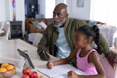 African american grandfather tutoring granddaughter using tablet and notebook at home