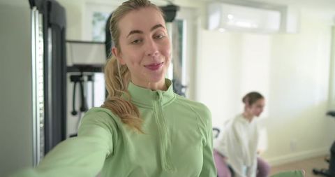 Friends recording selfie during home workout wearing pastel green zip-up