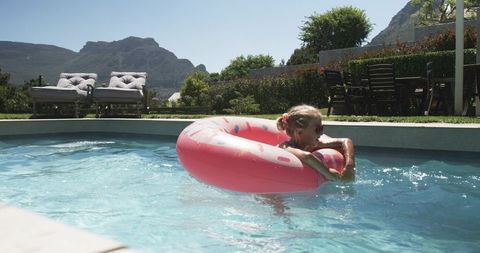 Little girl floating on pink donut pool float in sunny backyard with mountain view