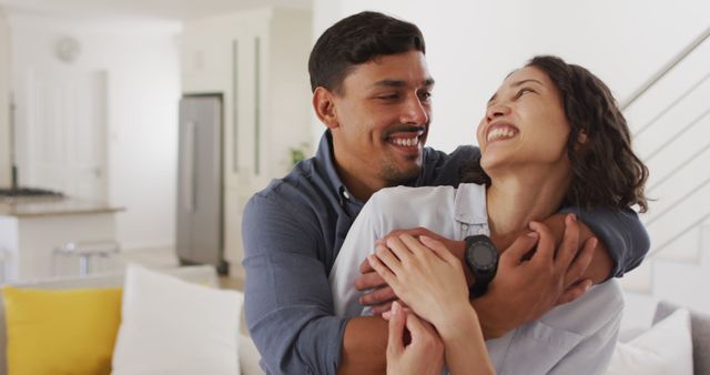 Couple embracing and smiling in modern living room. Use for illustrating romantic relationships, positive emotions, and lifestyle content. Suitable for blogs, articles, and social media focused on love, living spaces, and personal connections.