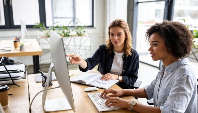 Two Female Colleagues Collaborating at Desktop Computer in Bright Modern Open-Plan Office