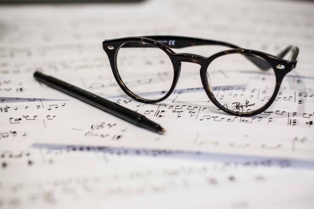 Black-framed glasses and a pen lying on sheets of music filled with musical notes. Ideal for use in articles or advertisements related to music composition, studying music, classical music practices, and the creative writing process.