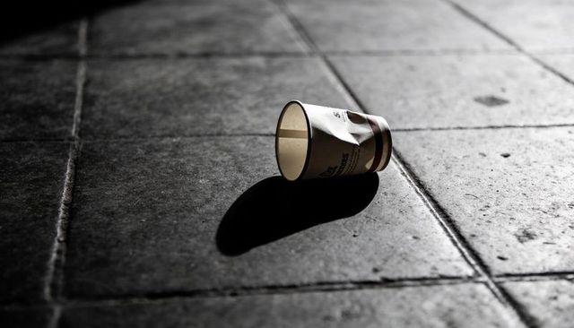 Crumpled paper cup casting long shadow on urban tiled floor at night