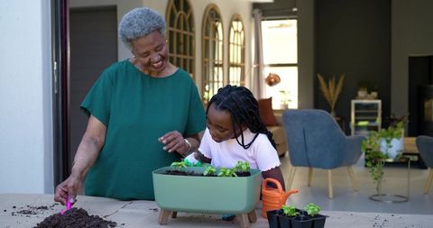 Grandmother and granddaughter planting seedlings together on home patio, gardening bond