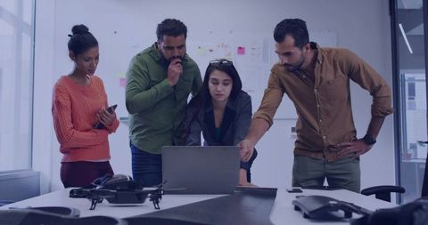 Multicultural team collaborating on drone prototype around laptop in modern startup office