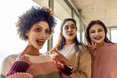 Diverse friends enjoying facial masks and wearing cozy knit sweaters in sunlit loft