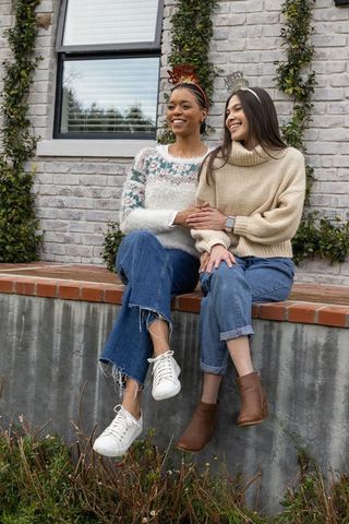 Smiling diverse friends celebrating on brick ledge wearing sweaters, jeans and crowns