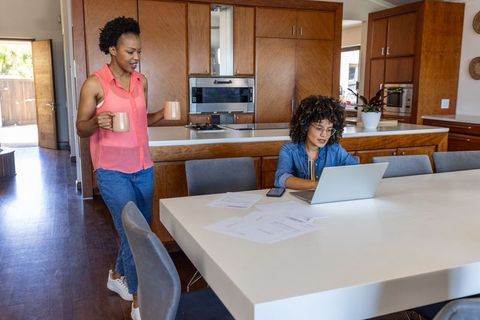 Mid-adult women collaborating at kitchen table with laptop and coffee for remote work