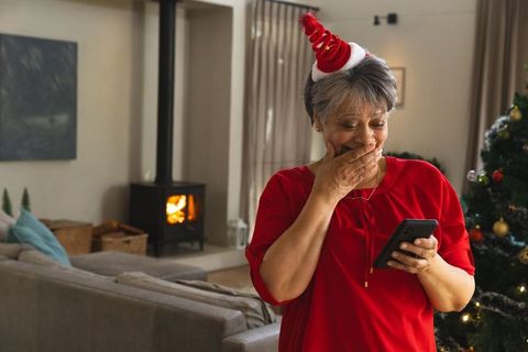Surprised senior woman with smartphone next to festive christmas tree