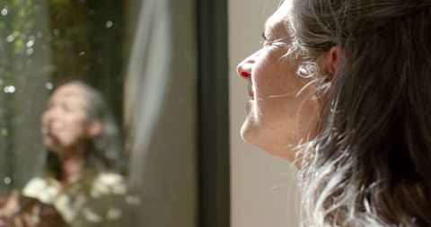 Mature Woman Looking Out Window in Reflection