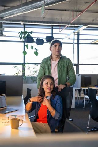 Young diverse coworkers collaborating in modern office with laptop and printed charts