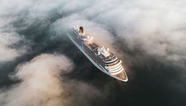 Gliding luxury cruise ship through morning fog with lit decks and lifeboats