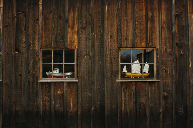 This image shows a rustic wooden wall featuring two windows with boat models inside. The weathered texture and warm tones add to the vintage and antique charm, suitable for use in design projects focusing on traditional craftsmanship, nautical themes, or rustic decor. Great for websites, advertisements, or articles about maritime history or decorative arts.