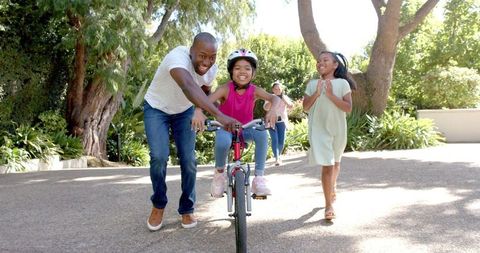 Father teaching daughter to ride bicycle in park setting