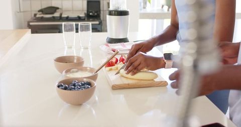 African american couple preparing fresh fruit breakfast on bright kitchen island