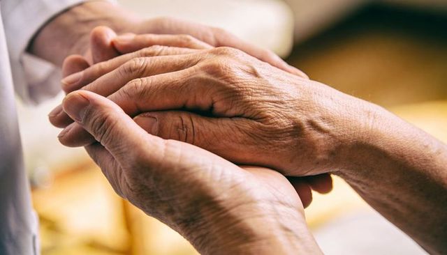 Caregiver holding hands cradling elderly wrist offering comfort and compassionate touch