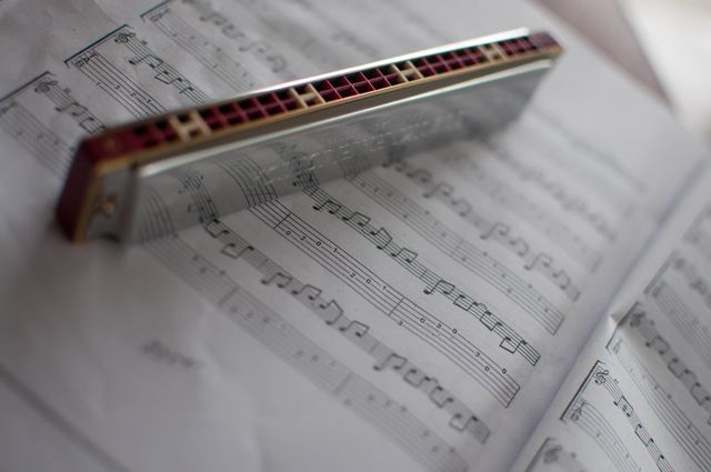 Close-up shows harmonica resting on open sheet music with clear musical notes, ideal for illustrating themes of music composition, practice, or learning. Useful for musicians, music educators, and instrument enthusiasts in educational or promotional materials.