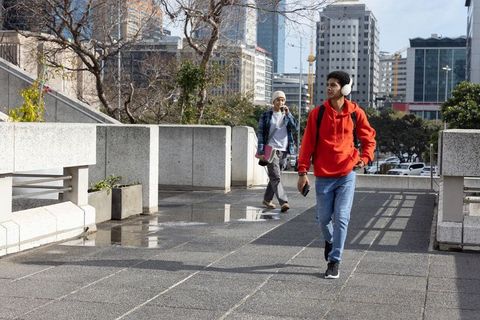 Students walking with headphones and smartphone on urban walkway near skyscrapers