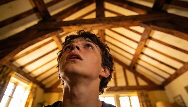 Teenager looking up catching warm sunlight in rustic home with exposed timber ceiling