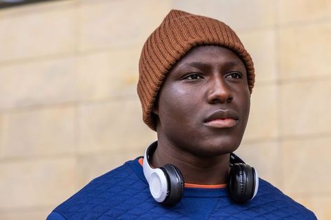 Young man wearing brown beanie and headphones looking thoughtful outdoors