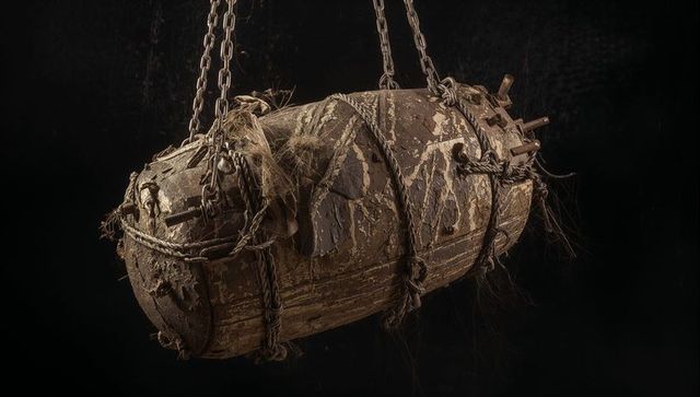 Corroded maritime cylinder suspended by chains and ropes showing rust and seaweed