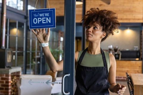 African american barista hanging open sign on urban cafe door, welcoming customers
