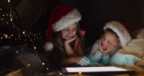 Children Wearing Santa Hats Relaxing with Tablet Under Fairy Lights