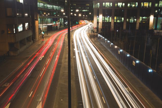 Long exposure shot capturing light trails of vehicles moving through the city street at night. Ideal for projects related to urban life, transportation, speed, modern cities, or dynamic city environments.