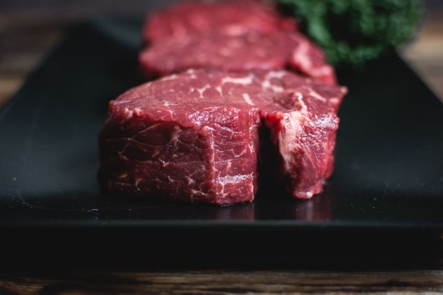High-quality image of fresh raw beef steaks placed on a black plate, ready for cooking. Perfect for food blogs, cooking websites, culinary magazines, and nutrition articles. Ideal for emphasizing the freshness and quality of ingredients in gourmet recipes and protein-rich meal plans.
