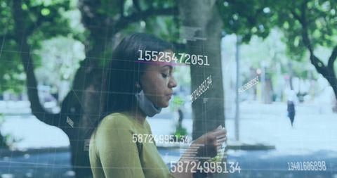 Futuristic numeric data overlay on smartphone in tree-lined park