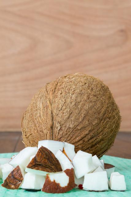 This image shows a close-up of a whole coconut and pieces of coconut placed on a green cloth. The background is a wooden surface. Ideal for use in food blogs, healthy eating articles, tropical fruit promotions, and organic food advertisements.