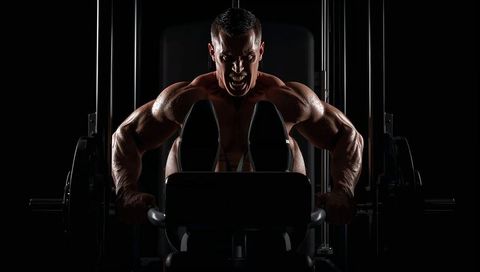 Explosive leg-press pushing muscular male athlete sweating under heavy resistance load