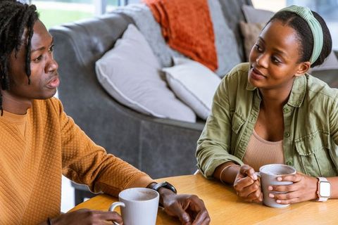 African american couple talking over coffee at wooden table, cozy living room conversation