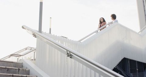 Two women talking and leaning on modern stair balustrade, urban high-key architectural