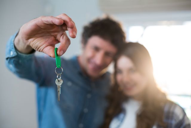 Happy couple holding a key, symbolizing new homeownership. Ideal for real estate promotions, home buying services, and advertisements targeting young families or first-time homebuyers.