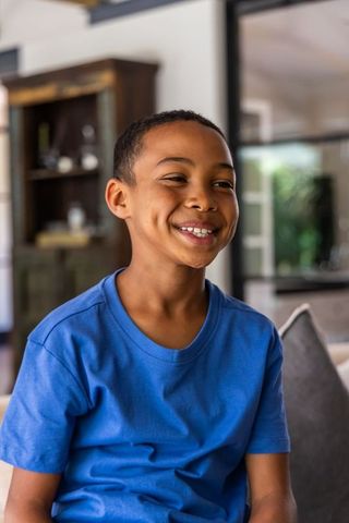 African american boy smiling on sofa in blue t-shirt enjoying bright sunlit living room
