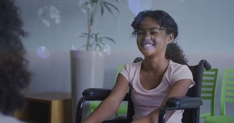 Smiling young girl in manual wheelchair talking with caregiver during clinic visit