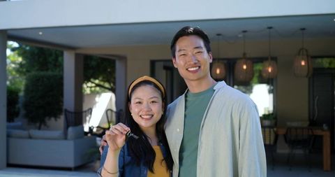 Young asian couple celebrating new home holding key on modern covered patio