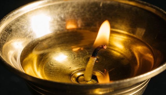 Glowing brass oil lamp with burning cotton wick reflecting warm amber light closeup