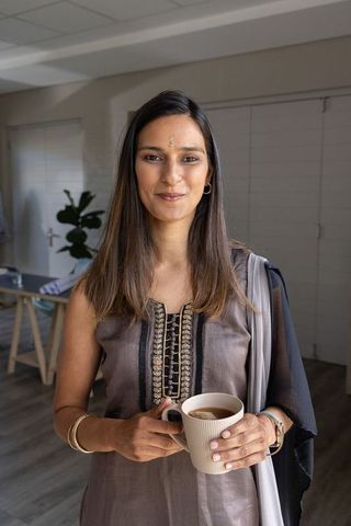 Indian woman standing at home holding ceramic mug wearing embroidered kurta and shawl