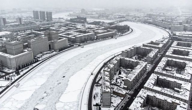 Winding frozen river snaking through snow-covered urban apartment grid, aerial winter cityscape